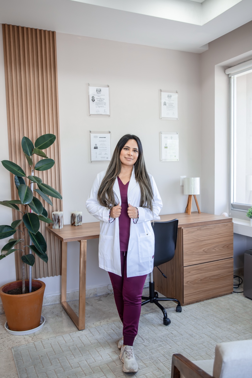 Dra. Anahí Gabriela Guerrero Reyna en su consultorio, con bata blanca y uniforme borgoña